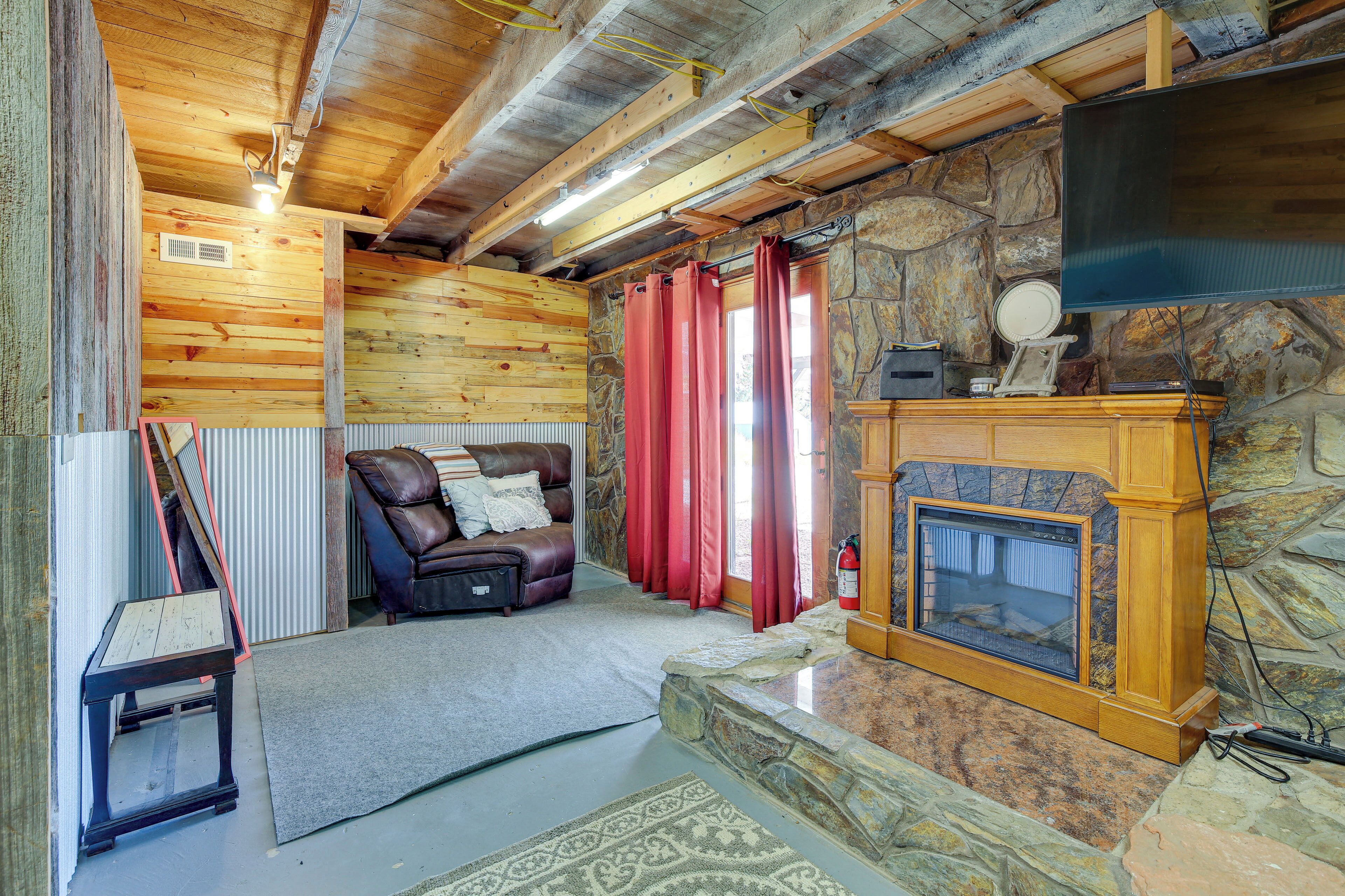 A cozy log cabin interior with a stone fireplace, a leather sofa, and a television mounted on the wall.