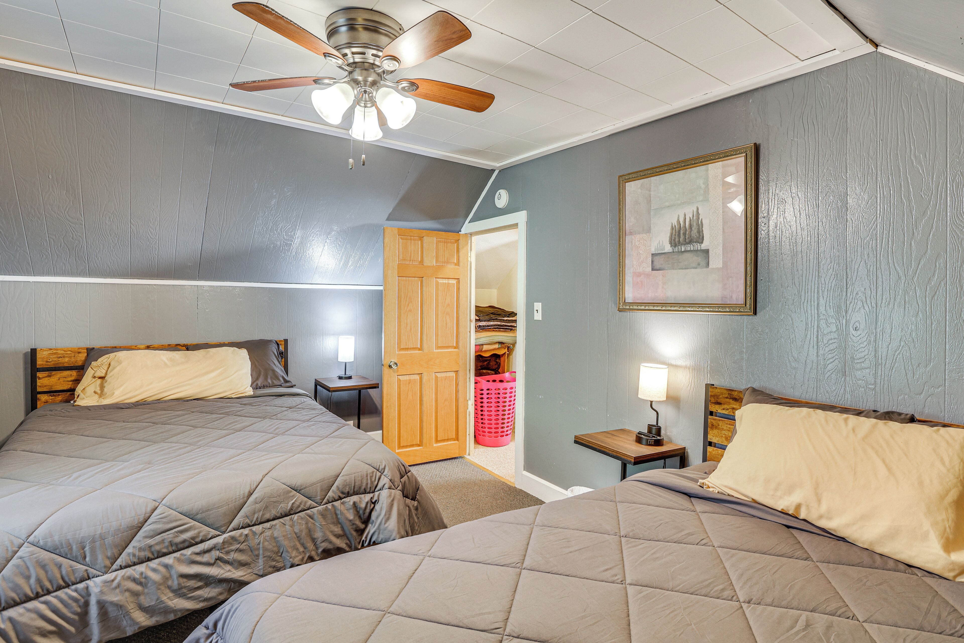 A bedroom with two beds, a ceiling fan, a framed picture on the wall, and a closet with a door.