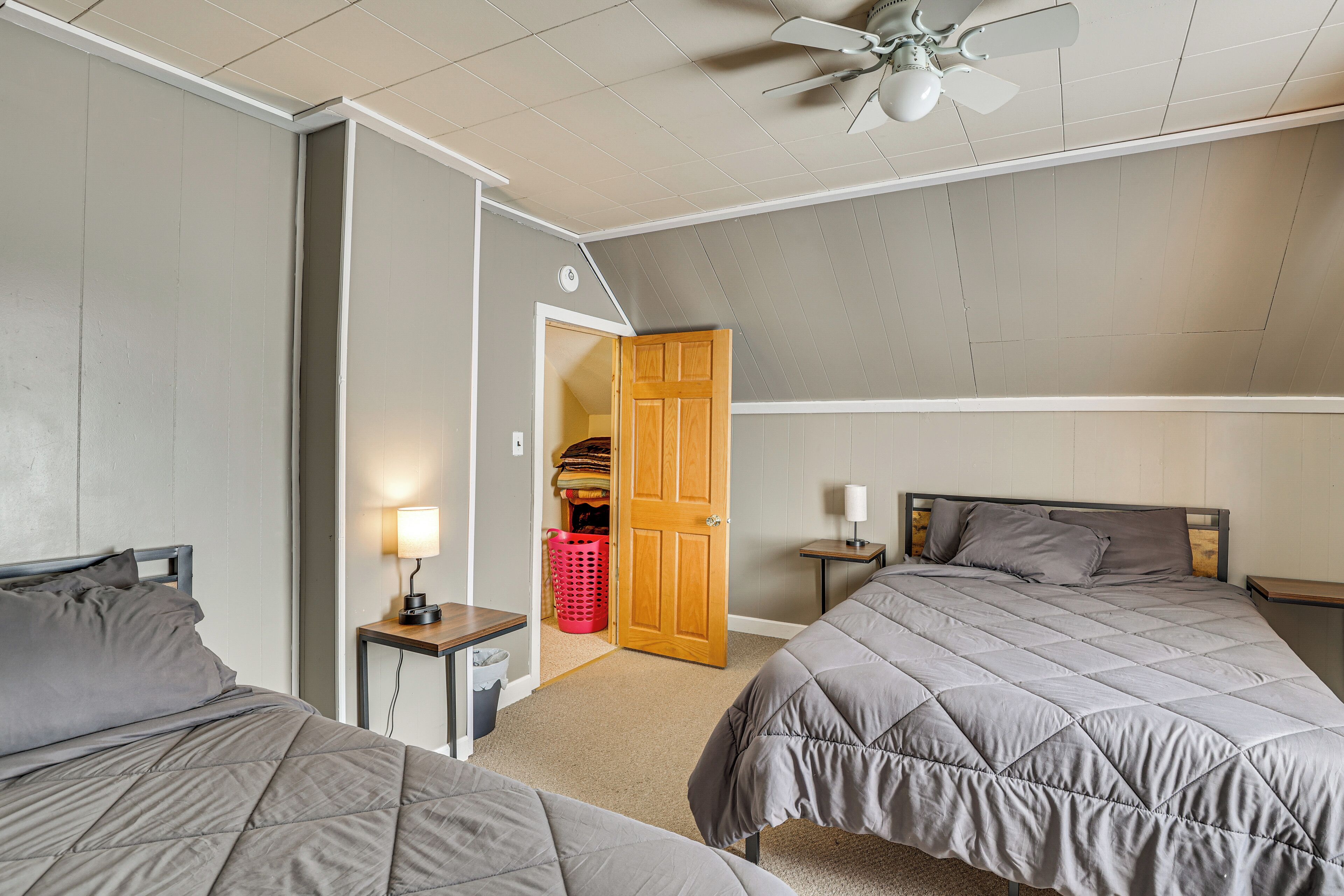 A bedroom with two beds, a ceiling fan, a nightstand with a lamp, and a closet with a door open.