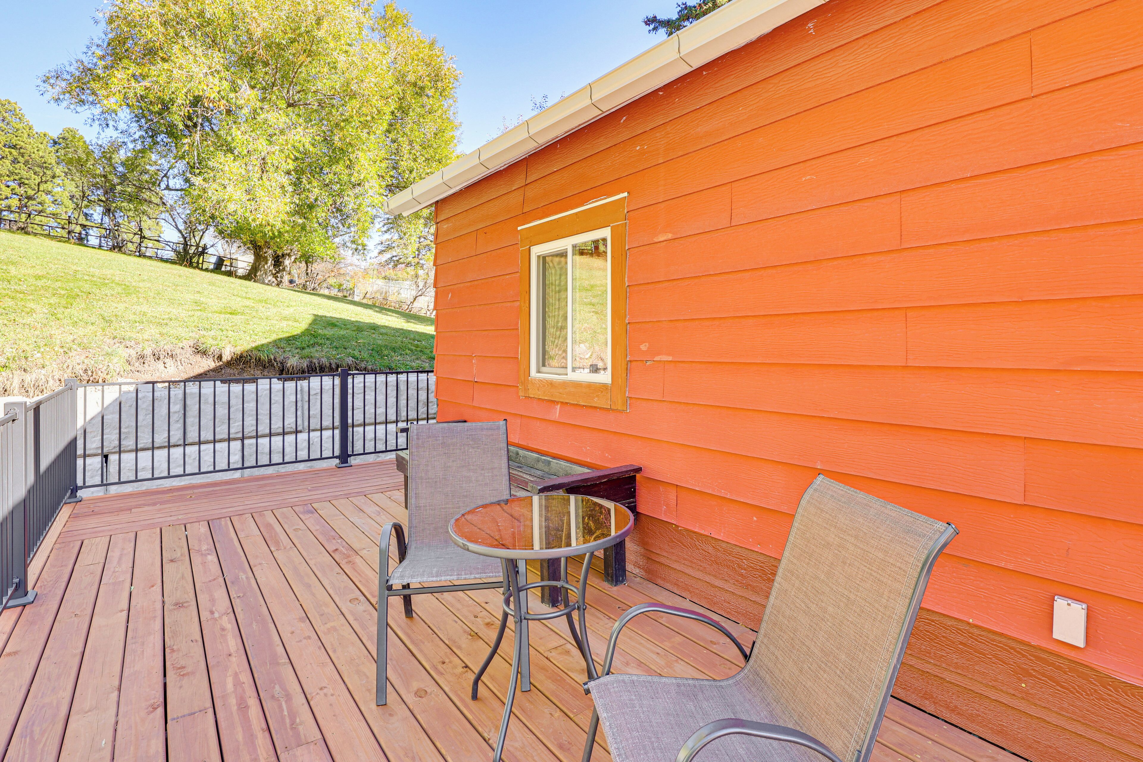 A wooden deck with metal chairs and a glass table, adjacent to an orange building with a window.
