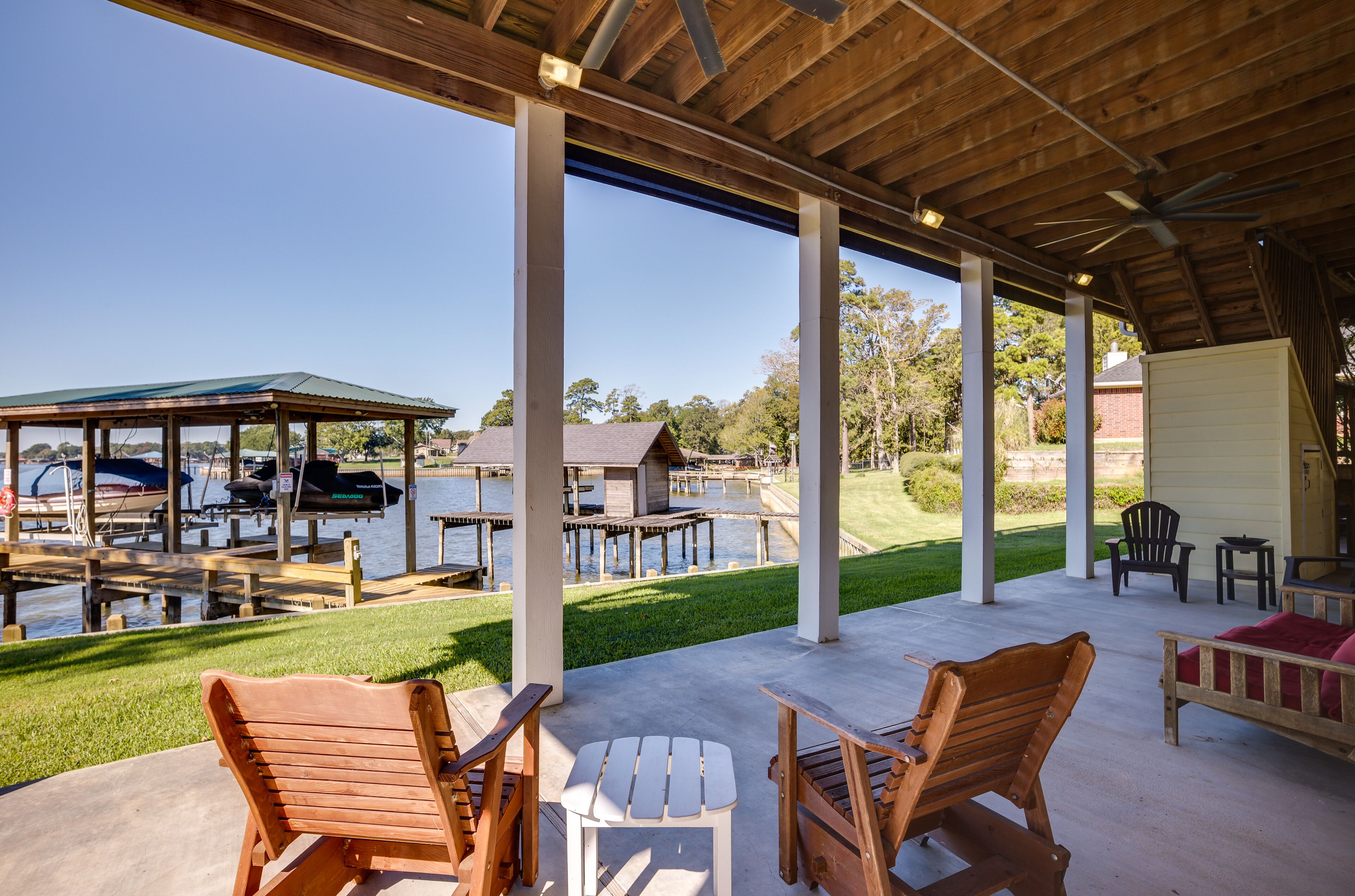 Un patio techado al aire libre con mobiliario de madera, una parrilla y vistas a un muelle con barcos.