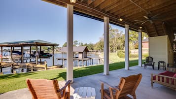 Un patio techado al aire libre con mobiliario de madera, una parrilla y vistas a un muelle con barcos.