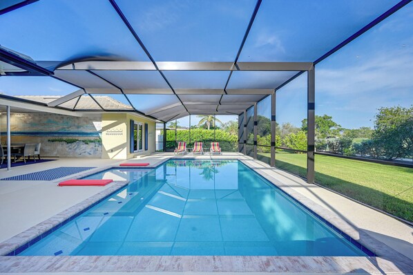 An indoor swimming pool with a clear view of the surrounding landscape, including a grassy area and trees.