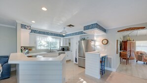 Una cocina moderna con armarios blancos, una isla central y un comedor con mesa y sillas de madera.