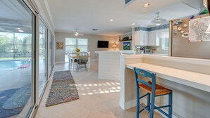 Una cocina moderna con una isla grande, muebles blancos y vistas del patio exterior.