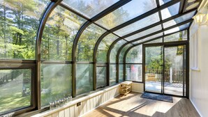Una veranda con ampie finestre in vetro, pavimento in legno e una panca.