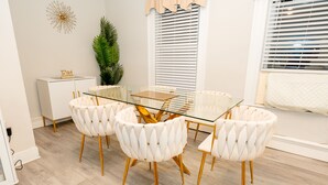 Un espace repas moderne avec une table en verre et des chaises blanches à revêtement et à pieds dorés.