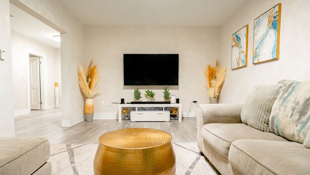 Un salon moderne avec un téléviseur à écran plat, un canapé beige, une table basse ronde et des plantes décoratives.