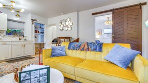 Una sala de estar con un sofá amarillo, una mesita de centro y una cocina al fondo.