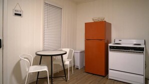 A small kitchenette with a white refrigerator, a white stove, and a small table with two chairs. - Sedona Retreat at La Hacienda (Wichita Falls)