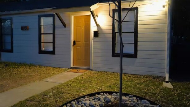 A single-story house with a front door, two windows with shutters, a small porch area, and a well-maintained lawn with a rock border. - Sedona Retreat at La Hacienda (Wichita Falls)