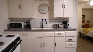 A compact kitchen with white cabinets, a microwave, a stove, and a sink. - Sedona Retreat at La Hacienda (Wichita Falls)