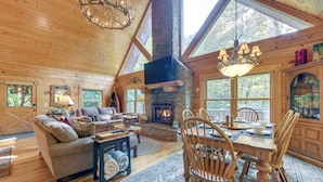 Un interior de cabaña acogedor con chimenea, muebles de madera y grandes ventanales.