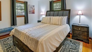 Une chambre à coucher avec un grand lit, deux tables de chevet, une petite table, un banc et un tapis à motifs.