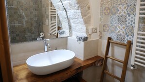 A bathroom with a white sink, a wooden vanity, a mirror, a towel rack, and patterned tiles on the walls. - Antico Monastero (Bitonto)