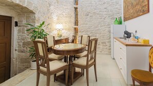 A rustic stone-walled room with a round wooden dining table and chairs, a potted plant, and a small side table with a lamp. - Antico Monastero (Bitonto)