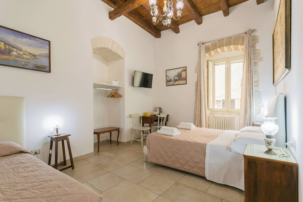 Un dormitorio con dos camas, un escritorio, una silla, un televisor y una ventana con cortinas.