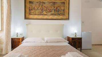 A hotel room with a large bed, two bedside tables, a wall-mounted painting, a bedside lamp, and a refrigerator.