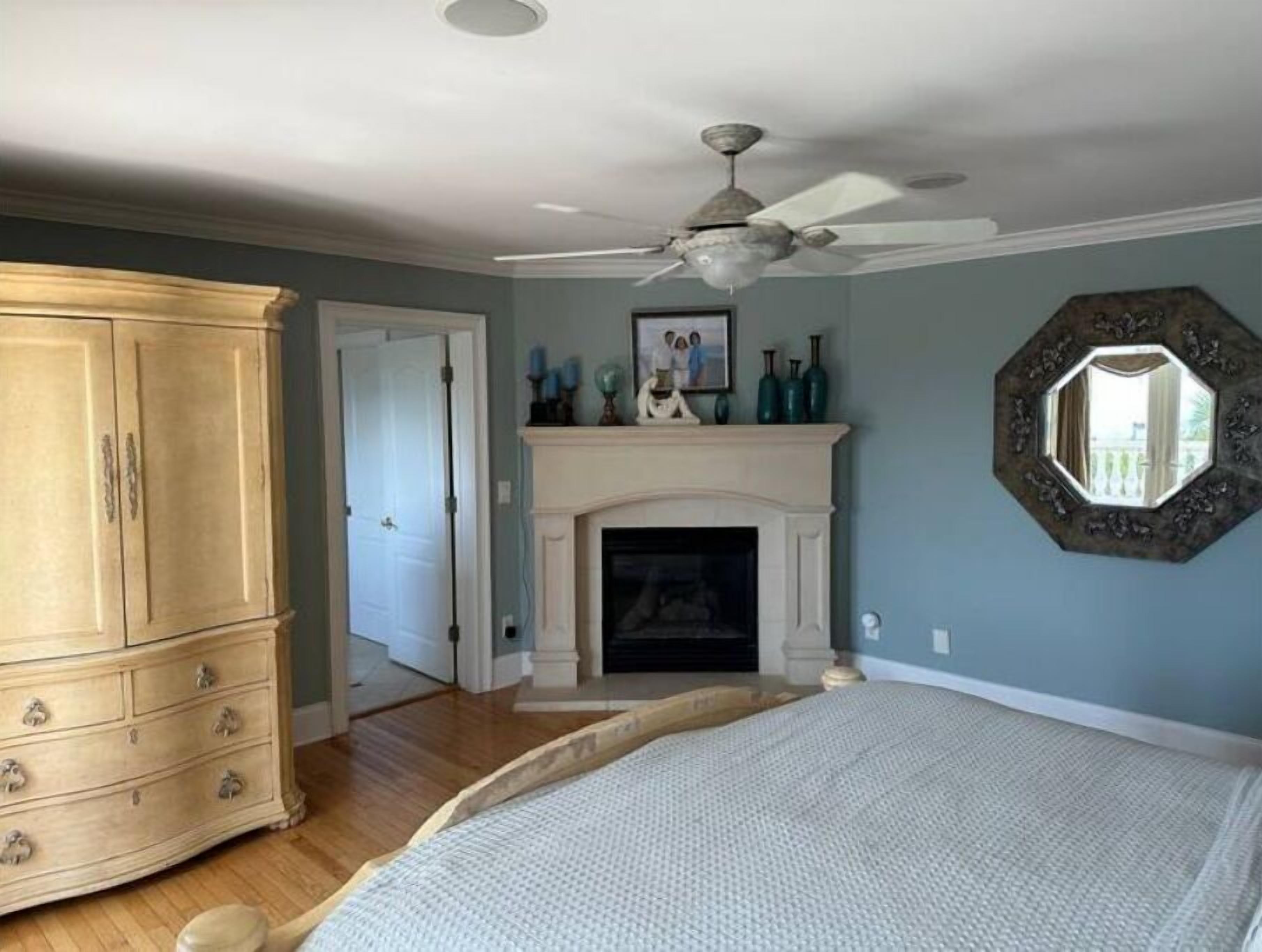 A bedroom with a large wooden wardrobe, a fireplace, a ceiling fan, and a decorative mirror.