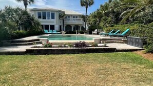 Une maison avec une piscine, entourée de palmiers et d’une pelouse bien entretenue.