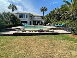 A house with a swimming pool, surrounded by palm trees and a well-maintained lawn.