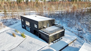Une maison moderne à deux étages, dotée d’un toit plat, de grandes fenêtres et d’un espace extérieur couvert.