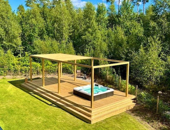 Une terrasse en bois avec un jacuzzi, située dans un jardin luxuriant et verdoyant.