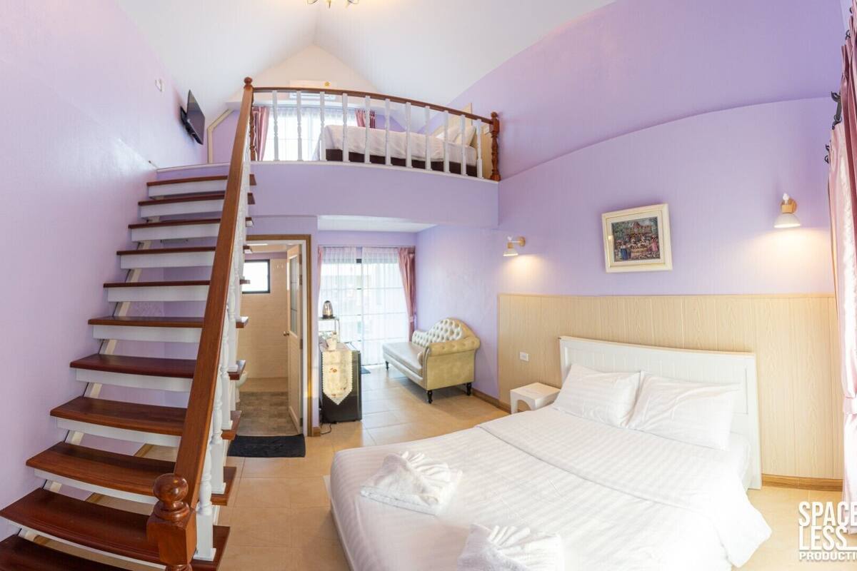 Un dormitorio con una cama doble, una escalera curva, una silla y un cuadro en la pared.