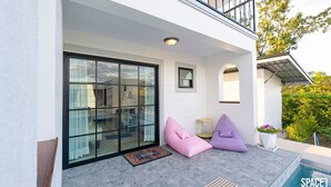 A modern house with a glass door leading to a patio area. There are two bean bags and a small round table on the patio. - The Autumn Creek ChiangRai (Chiang Rai)