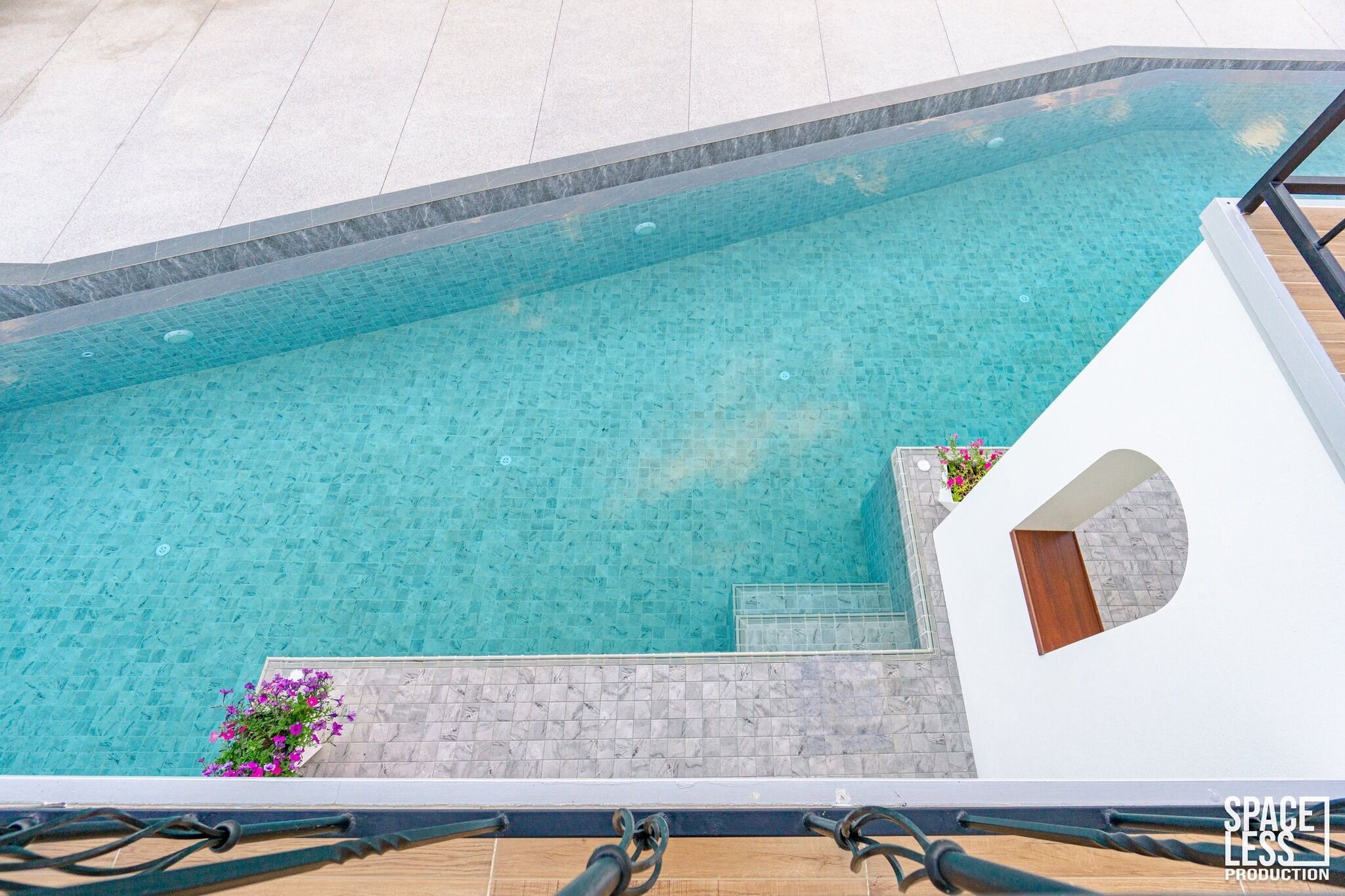 Ein klares, blaues Schwimmbecken mit gefliestem Rand, Stufen zum Wasser und eine weiße Wand mit einem Fenster.