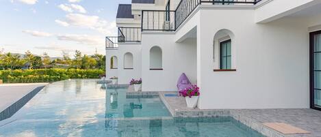 Ett modernt hus med en swimmingpool, vit fasad och en balkong med ett metallräcke.