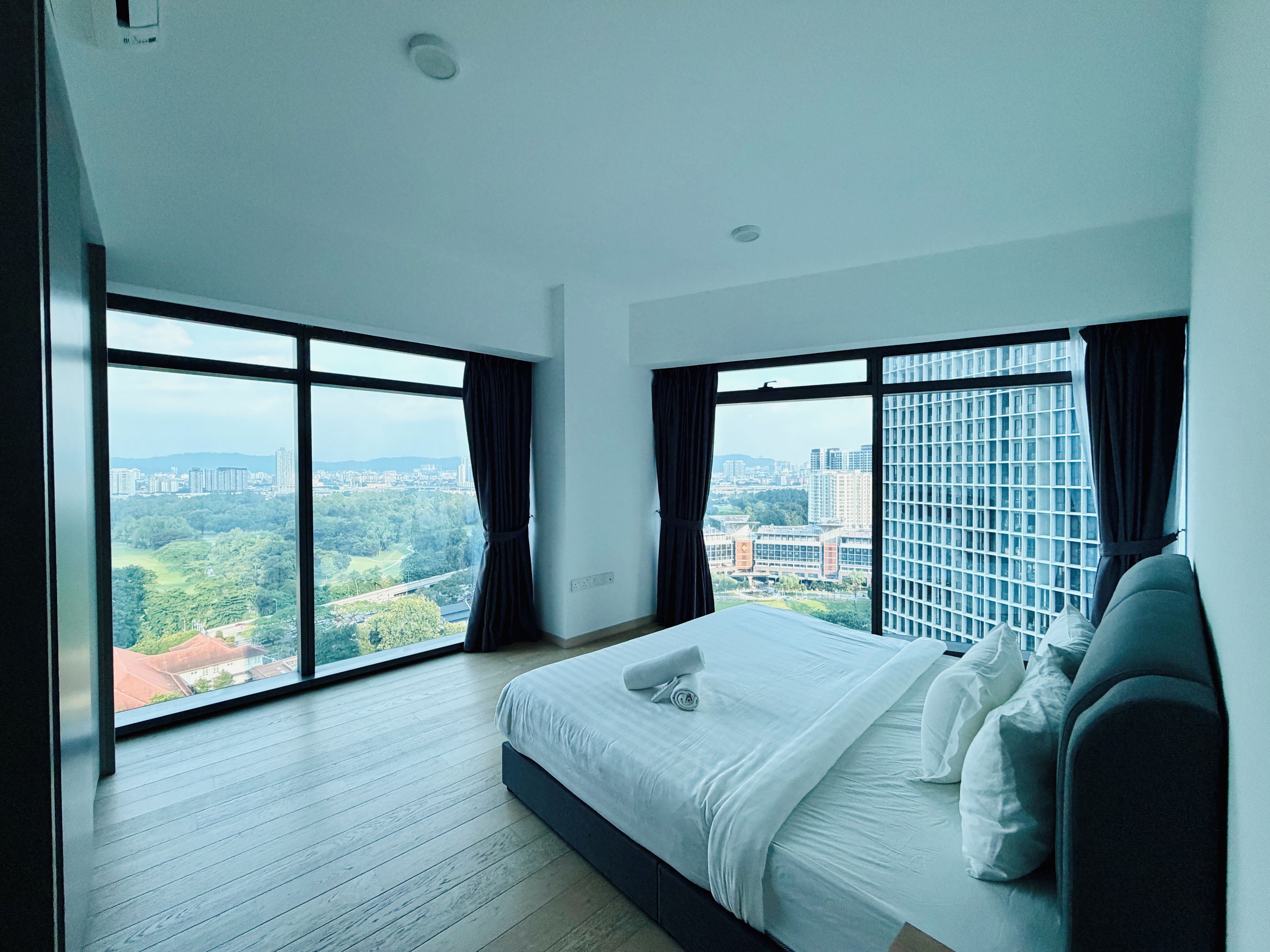 A modern hotel room with a large bed, two windows, and a city view.
