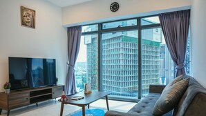 A modern living room with a large flat-screen TV, a sofa, a coffee table, and a view of a cityscape through large windows. - Eaton Residence KLCC By Flixses (Kuala Lumpur)
