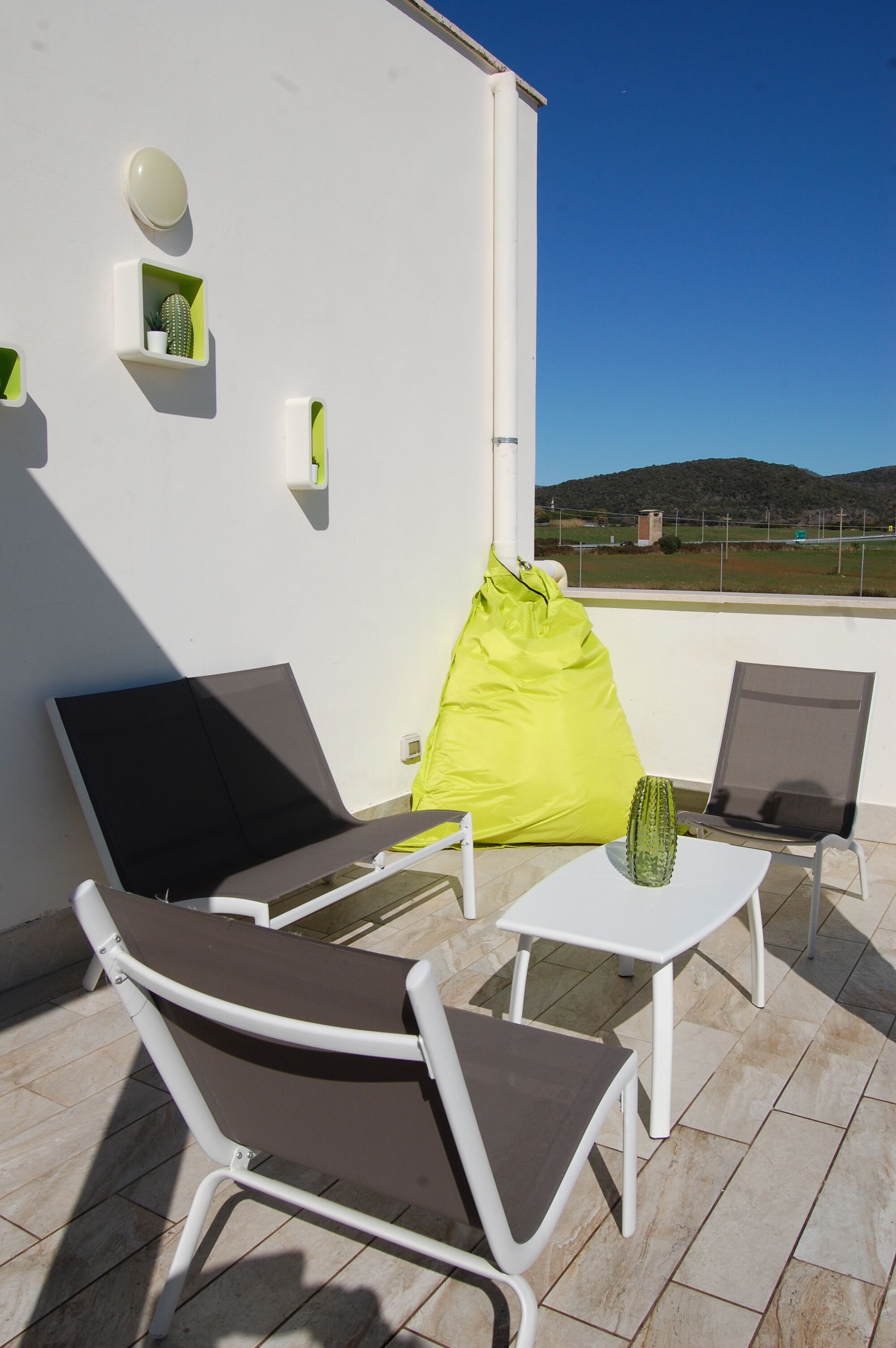 A balcony with two lounge chairs, a small table, and a green bean bag.