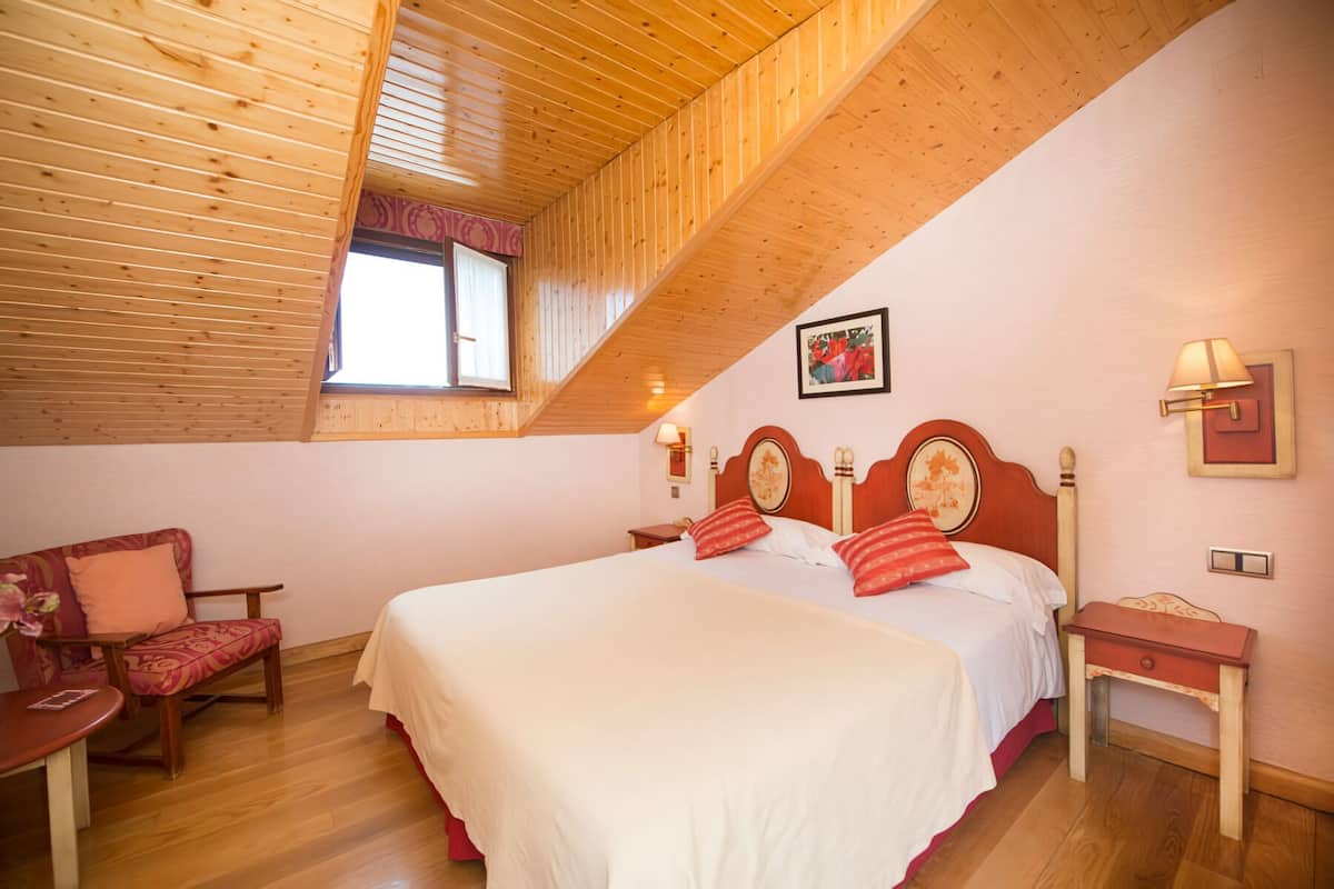 Une chambre avec un plafond en bois, un lit avec des oreillers rouges, une chaise, une table de chevet et une lampe fixée au mur.