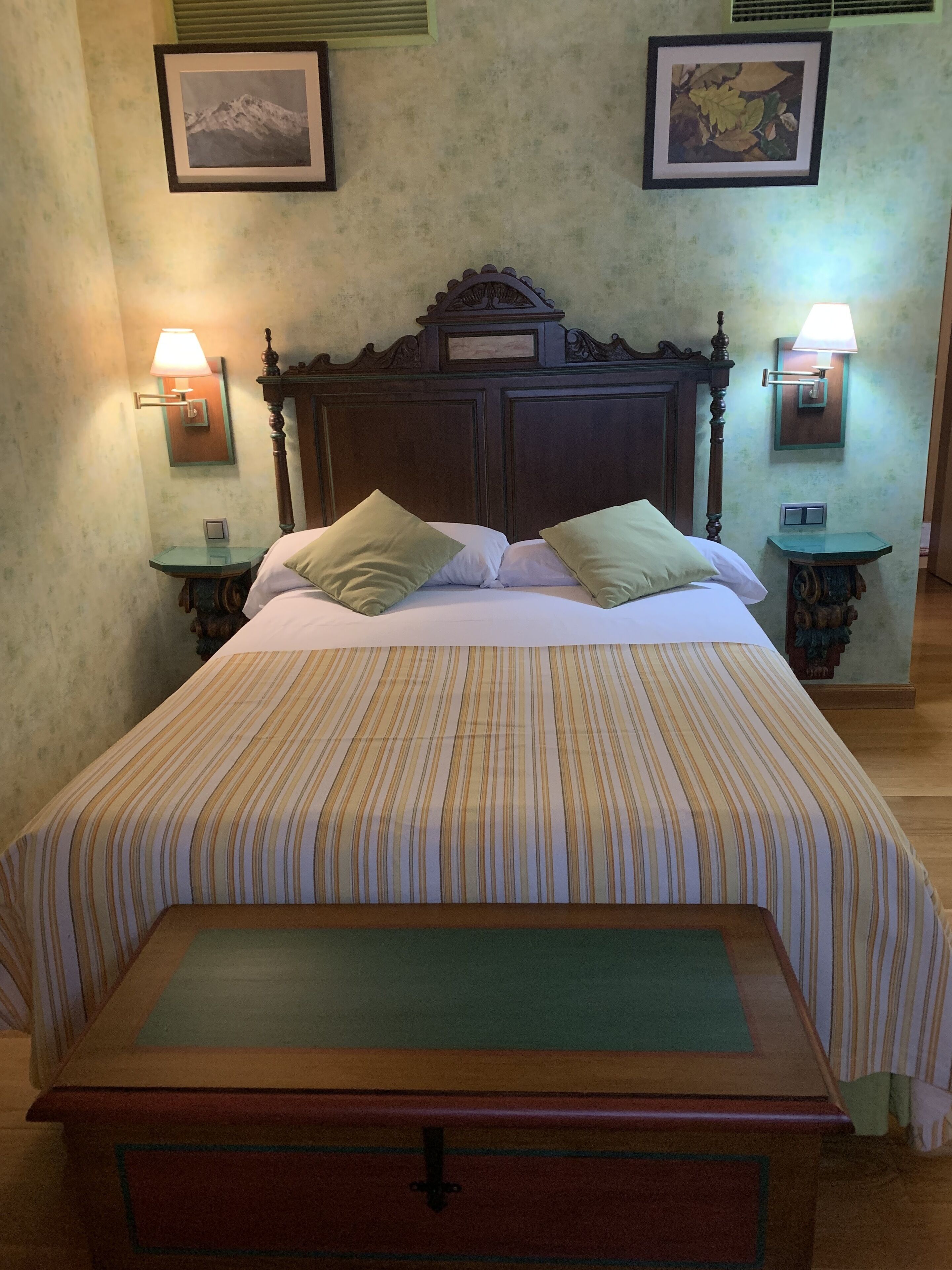 Una cama bien hecha con ropa de cama a rayas, un cabecero de madera, dos mesitas de noche con lámparas y cuadros en las paredes.