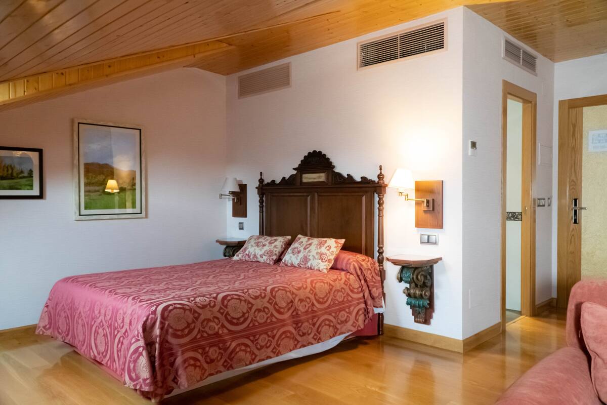 Une chambre à coucher avec un lit en bois, une table de chevet, une lampe fixée au mur et une porte.