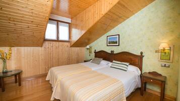 Un dormitorio con techo de madera, una cama con ropa de cama a rayas, una mesita de noche, una lámpara de pared y una ventana con cortinas.