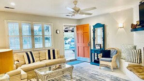 A spacious living room with a beige sofa, a wicker coffee table, a blue chair, and a large mirror. - Endless Beach #A (Virginia Beach)