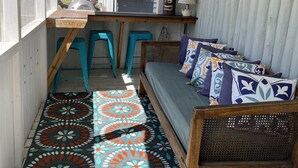 A small, enclosed cabin with a wooden bench, turquoise stools, a patterned rug, and a bed with colorful pillows. - Canary Cottage: Lakeside, Boat Slip, Beach, Family Friendly (Ludington)