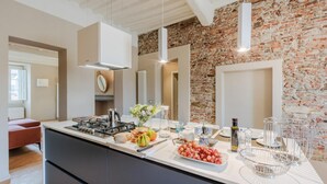 A modern kitchen with a central island, a brick wall, and pendant lighting. - Casa Pino in Lucca With 2 Bedrooms and 2 Bathrooms (Lucca)