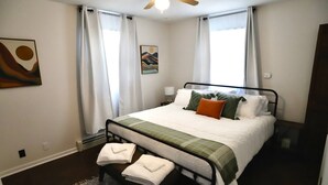 A bedroom with a bed, white curtains, a ceiling fan, and a painting on the wall. - 2BR/1BA Cozy Retreat near Timberline slopes (Davis)