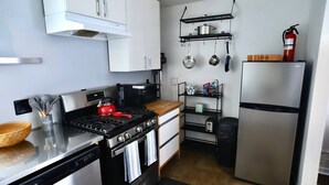 A compact kitchen with a stove, oven, dishwasher, and a refrigerator. There are shelves above the stove holding pots and pans. - 2BR/1BA Cozy Retreat near Timberline slopes (Davis)