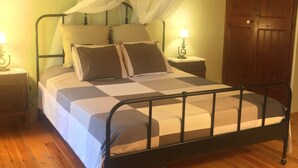 Ein Bett mit Metallgestell, Holzboden, Holztür und ein Nachttisch mit Lampe.