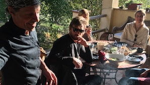 Eine Gruppe von Menschen versammelt sich um einen Grill im Freien, mit Speisen und Getränken auf dem Tisch.