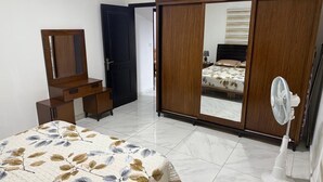 Une chambre à coucher comprenant un lit, une commode, une armoire et un ventilateur sur pied.