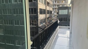 Un balcon doté d’une rambarde en métal noir, d’un sol carrelé et offrant une vue sur les bâtiments voisins.