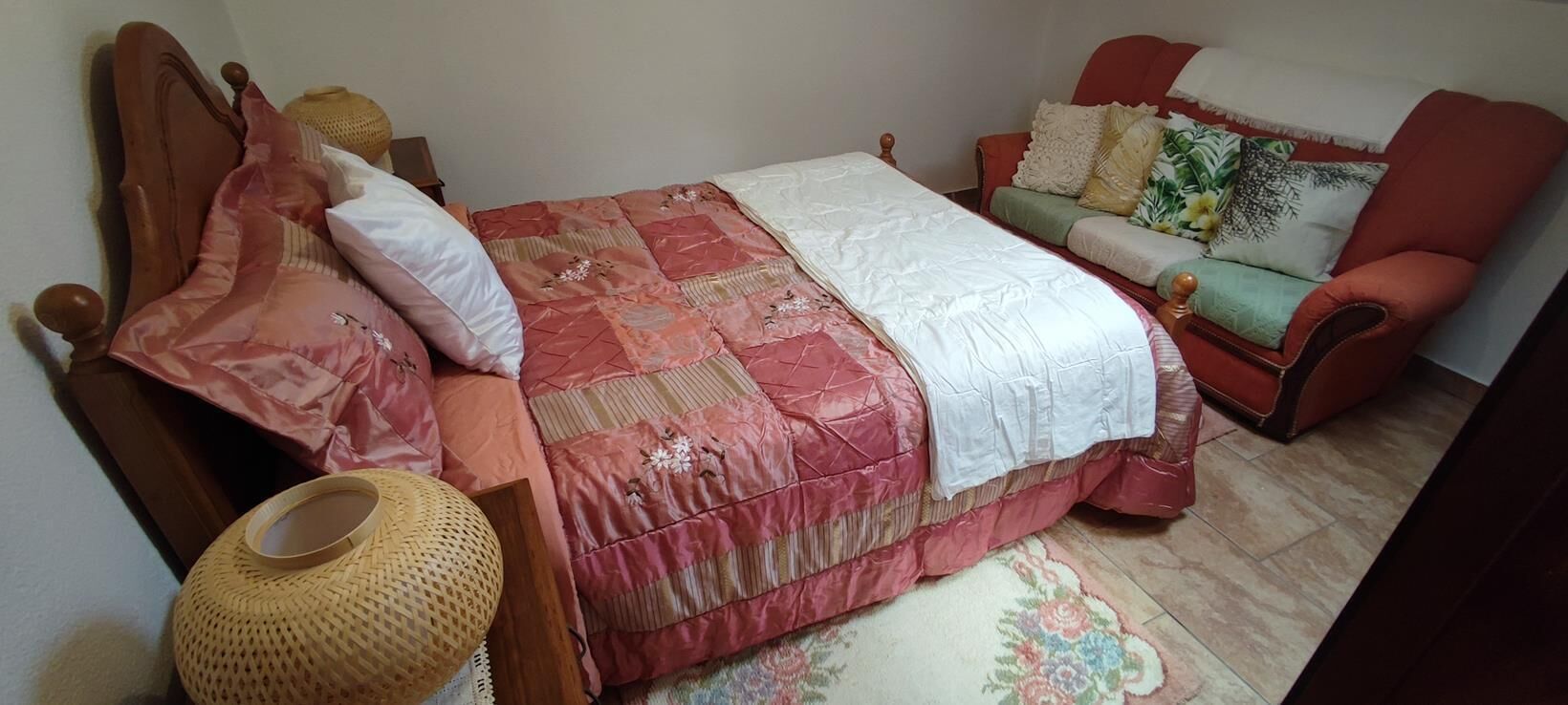 A bedroom with a wooden bed, a red sofa, and a woven basket.