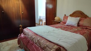 Ein Schlafzimmer mit einem hölzernen Bett, einem Nachttisch, einer Lampe und einem Sessel.