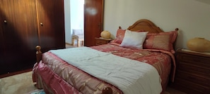 Ein Schlafzimmer mit einem hölzernen Bett, einem Nachttisch, einer Lampe und einem Sessel.